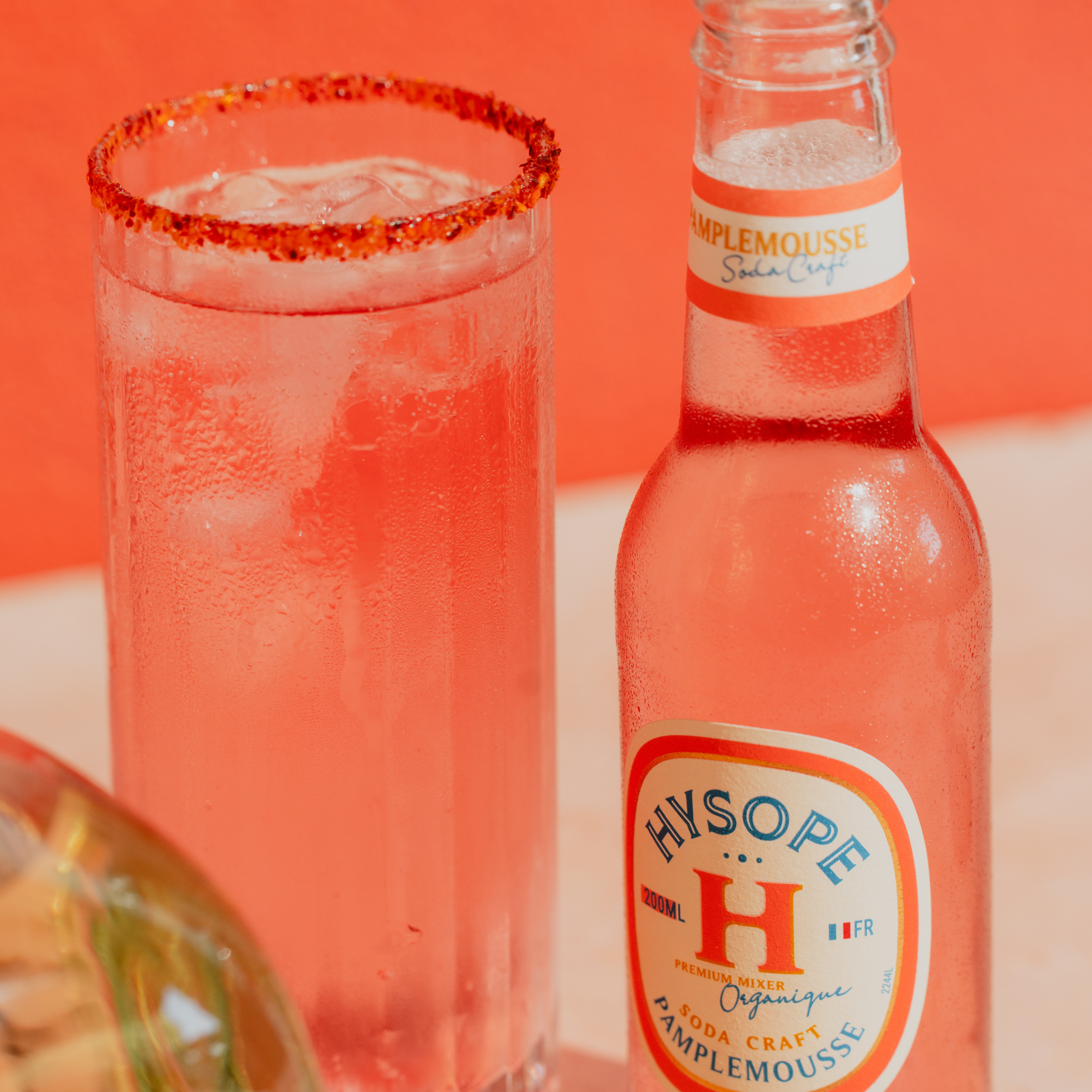 Verre de cocktail Paloma au pamplemousse rose à côté d'une bouteille de soda français Hysope